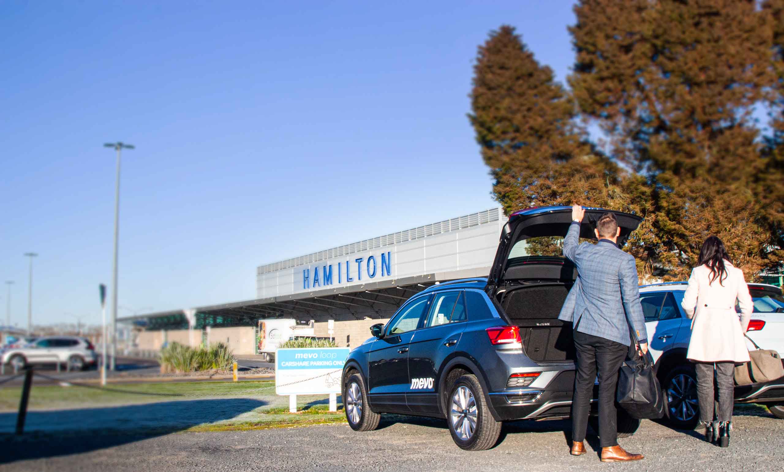 Man and woman outside Hamilton airport unloading their bags from a Mevo vehicle