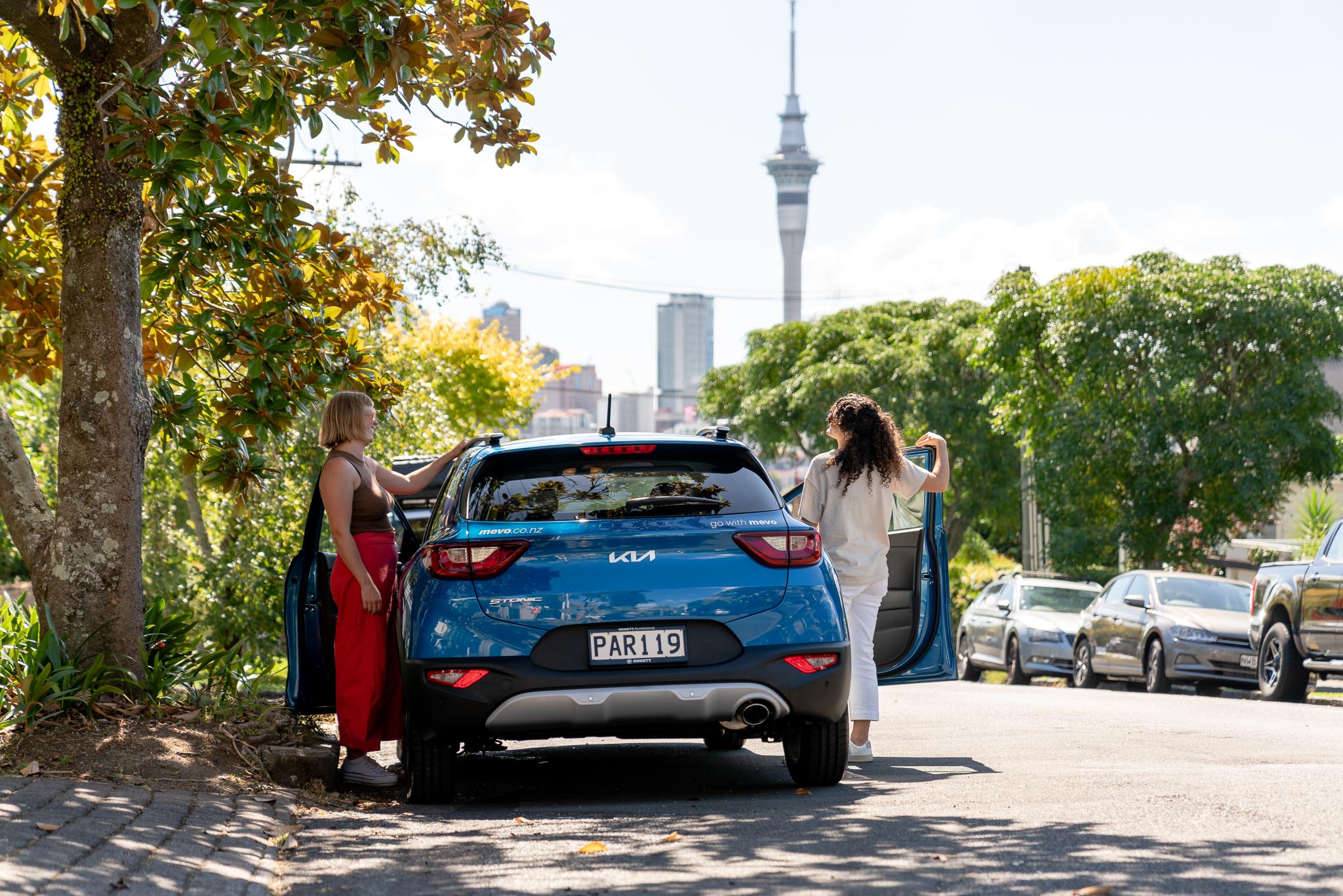Two women getting into a Mevo car in Ponsonby, Auckland. The Sky Tower can be seen in the background.