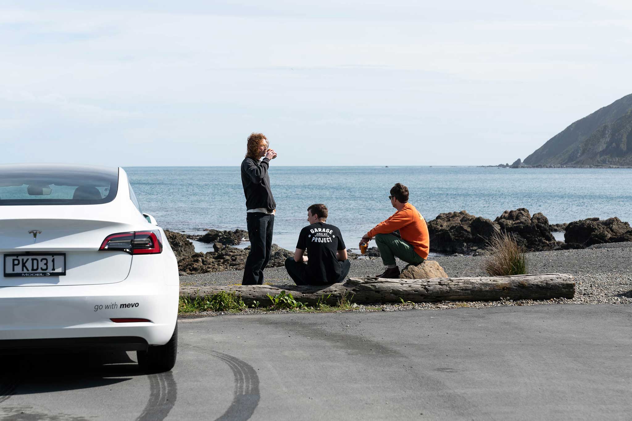 Three of the Garage Project team sitting next to a Mevo vehicle by the seaside.
