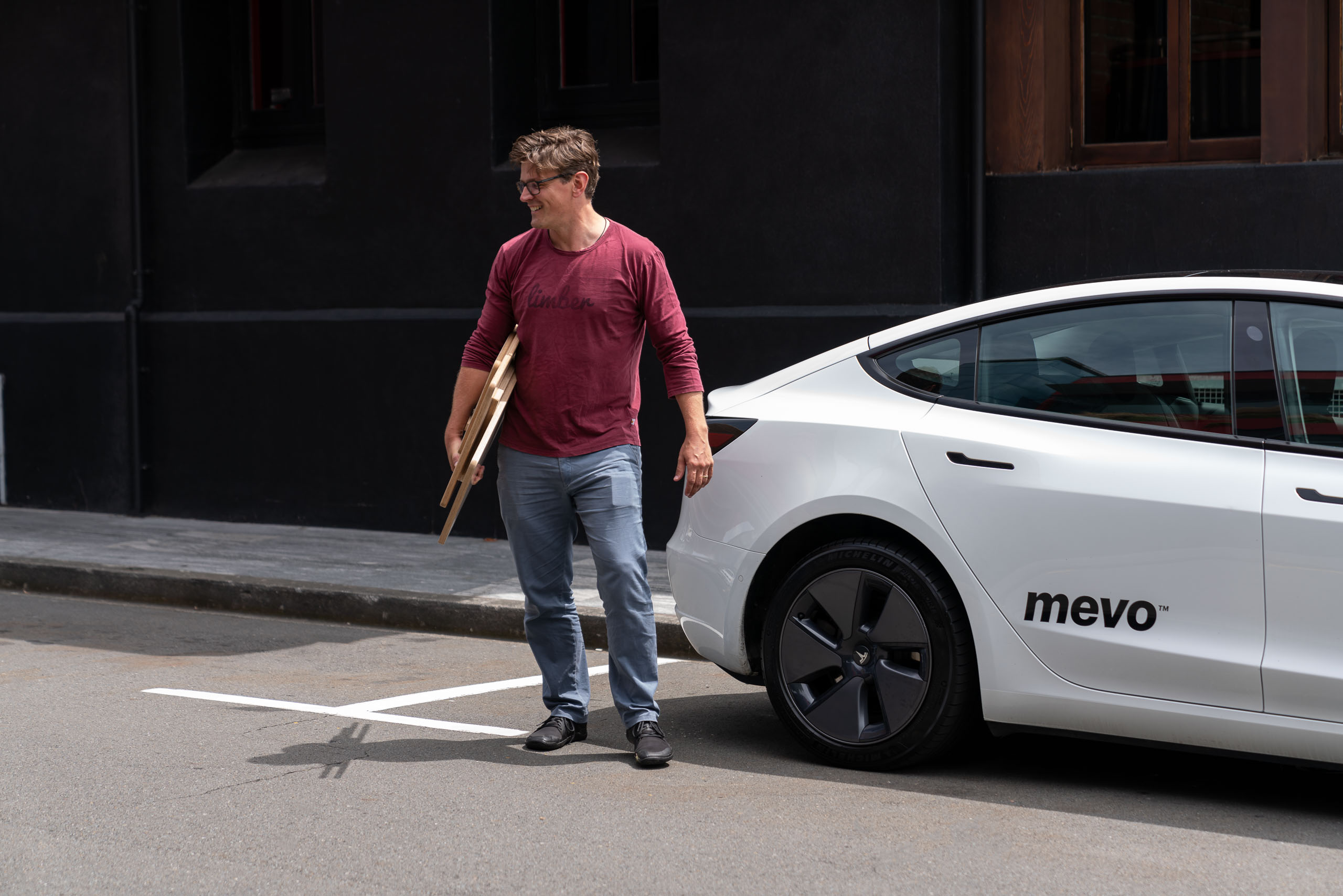 Bart standing next to a Mevo vehicle on the Wellington streets. He is holding a Limber Mini desk, folded up.